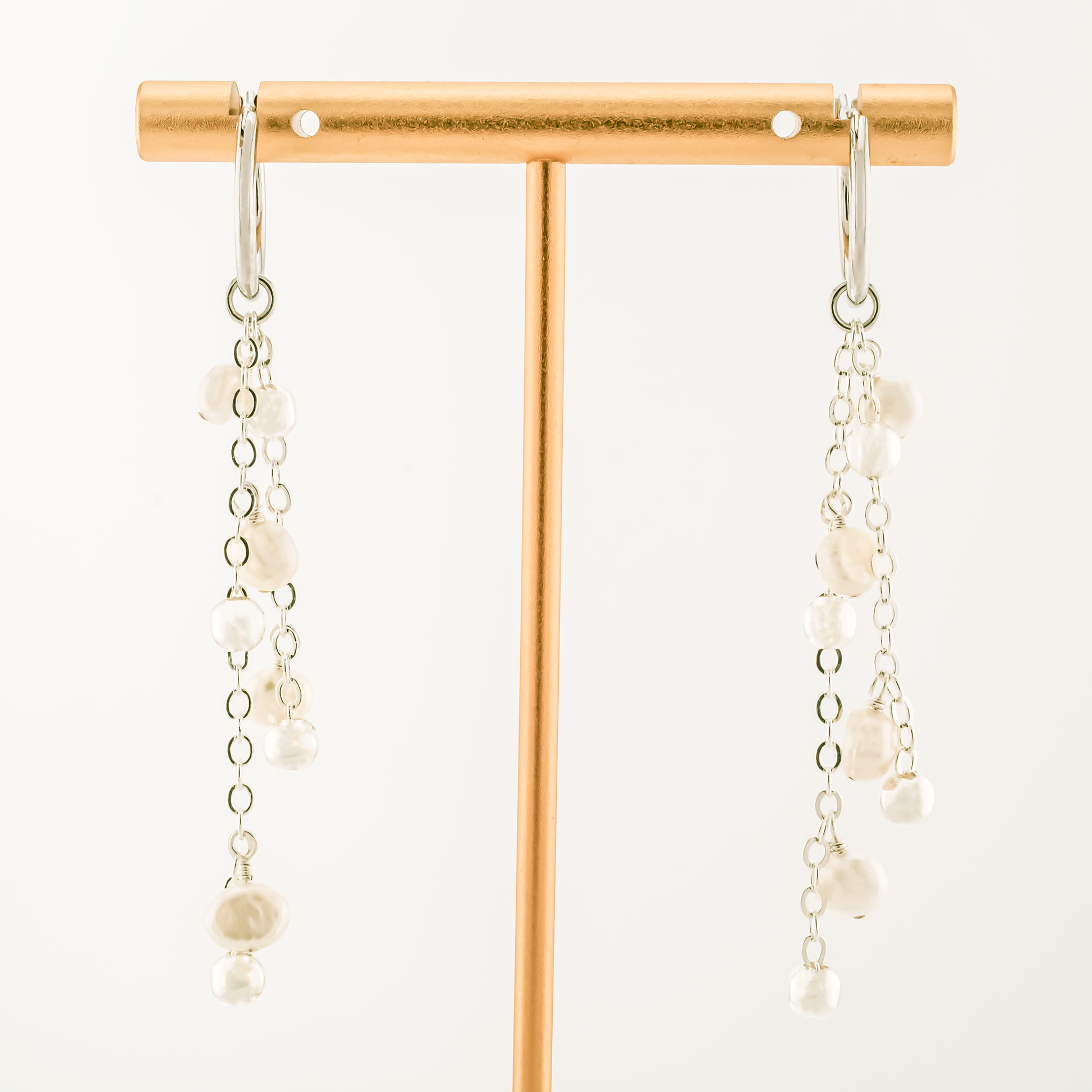 pair of earrings with detachable charm of baroque pearls on silver chains on a white background.